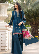 Woman in a teal traditional outfit with pink accents standing outdoors.